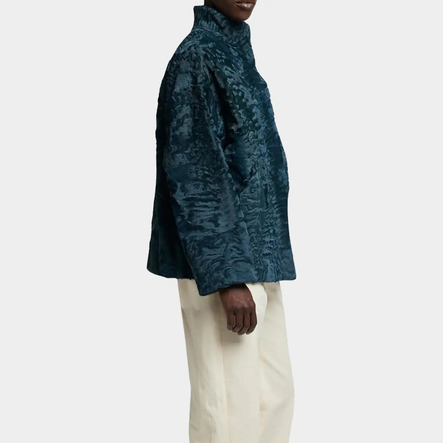 Person wearing a textured teal jacket and white pants on a light gray background
