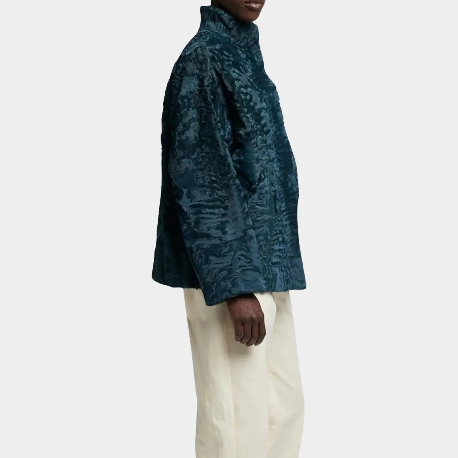 Person wearing a textured teal jacket and white pants on a light gray background