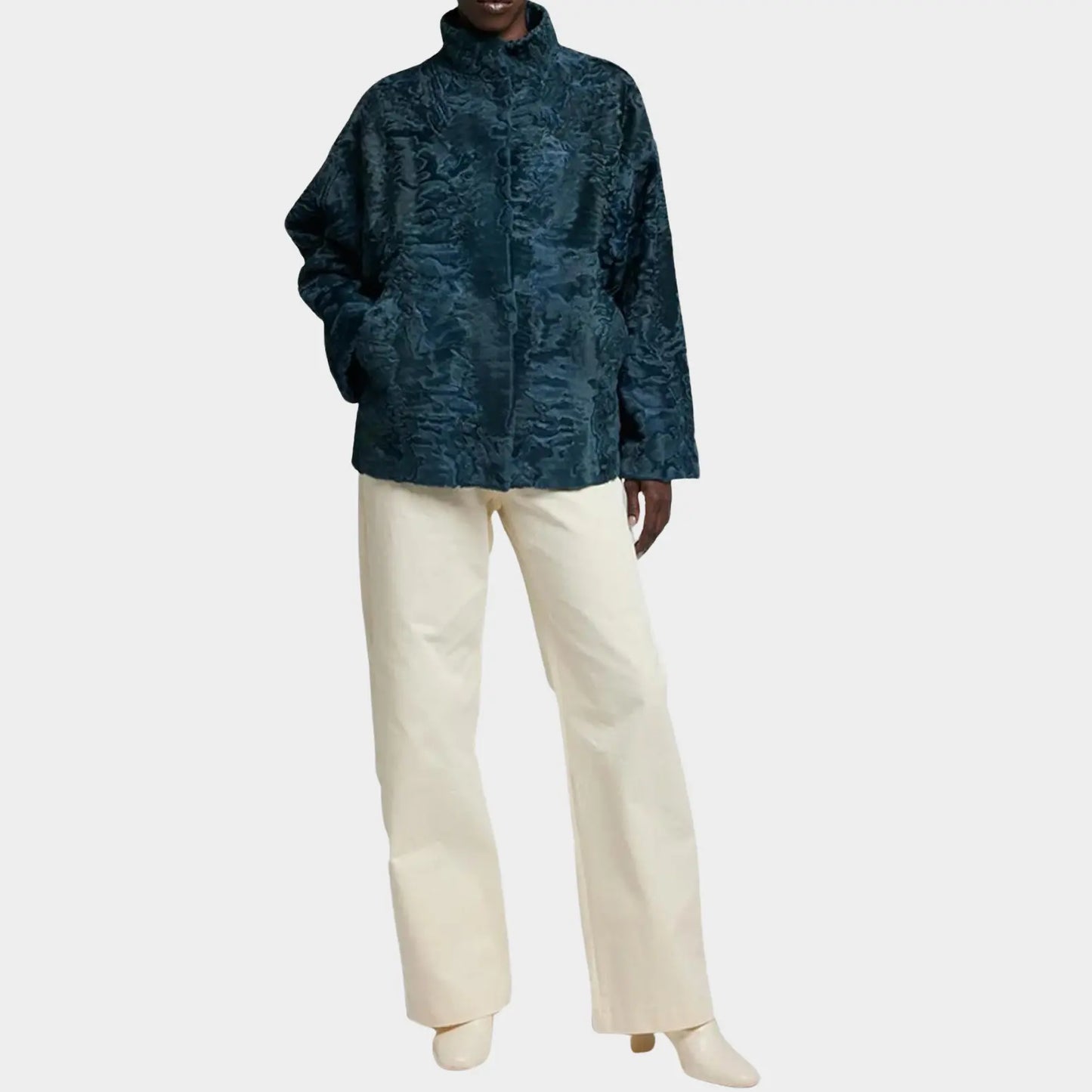 Person wearing a teal textured jacket and white pants on a white background