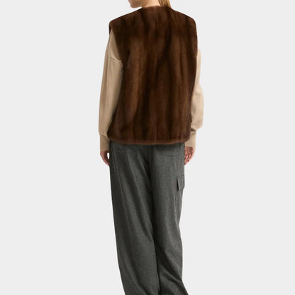 Person wearing a brown fur vest over a beige shirt with gray pants on a white background