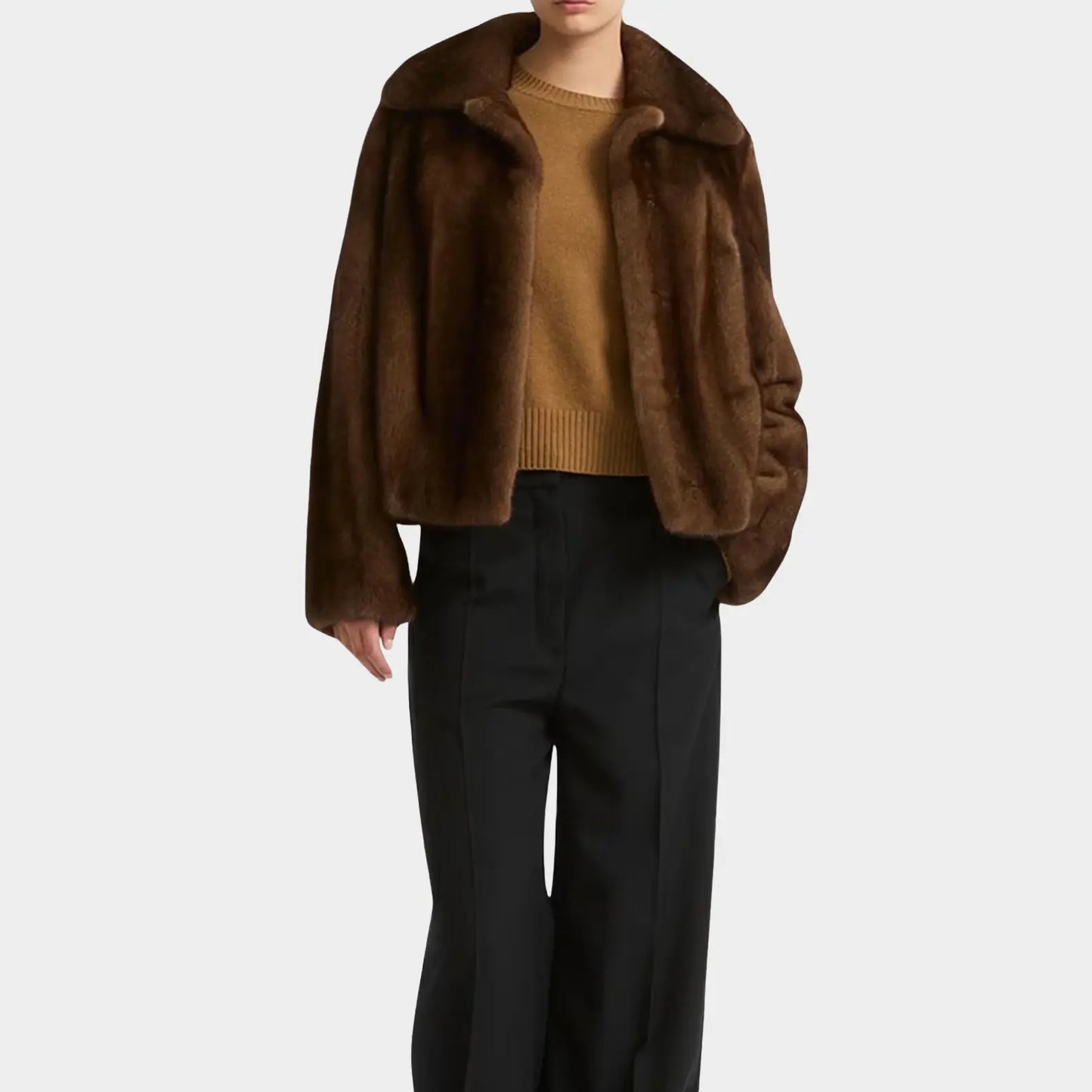 Person wearing a brown fur coat, mustard sweater, and black pants on a white background