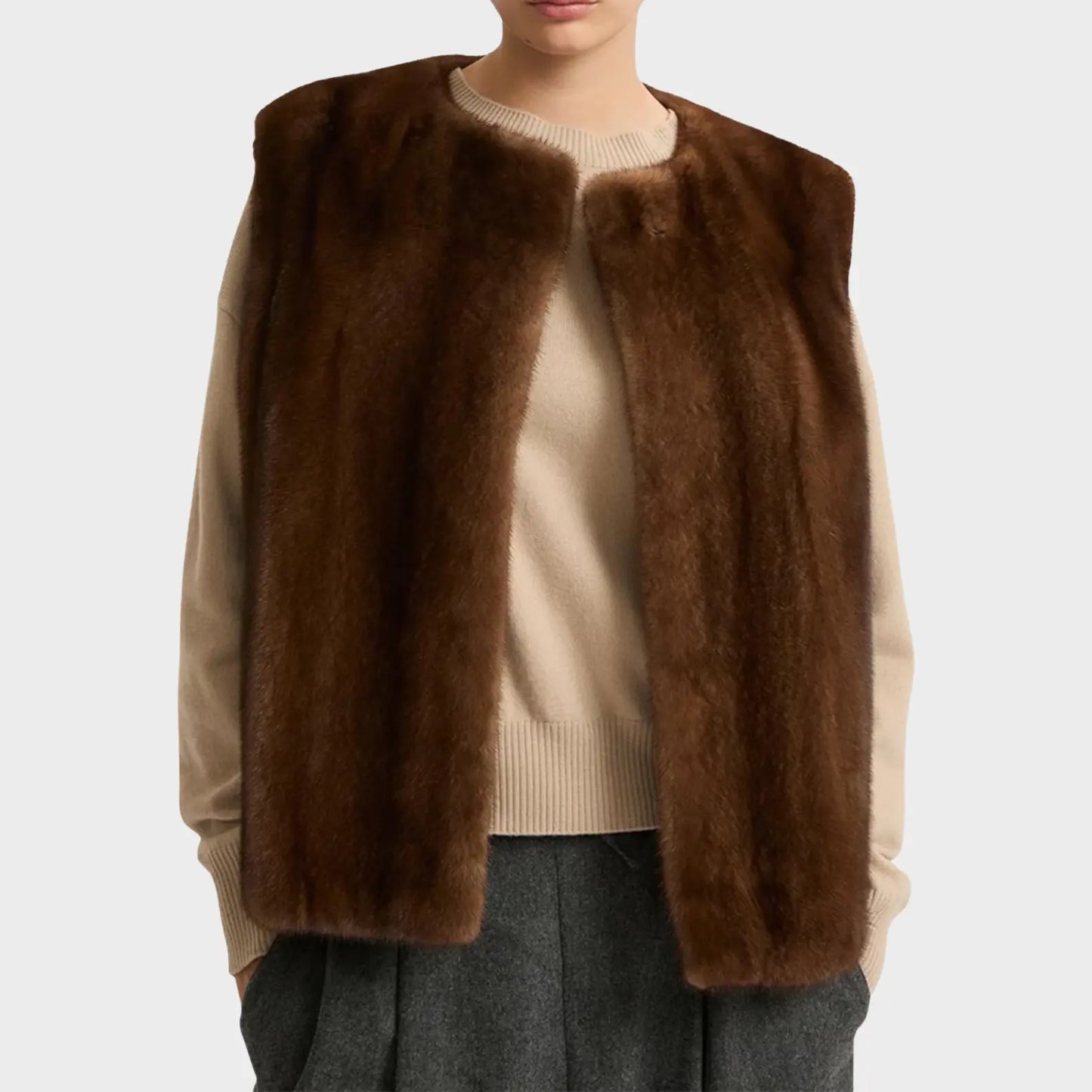 Brown fur vest over a beige sweater and gray pants on a white background
