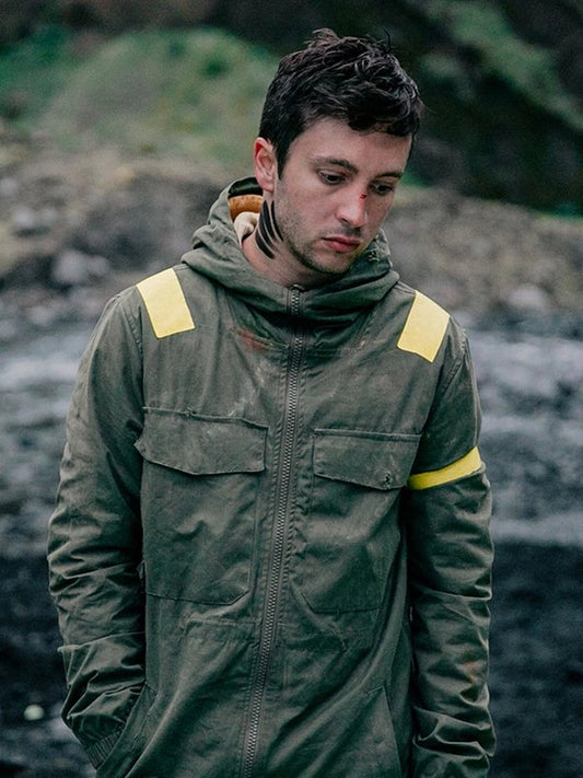 Man wearing a green jacket with yellow accents standing on a rocky terrain