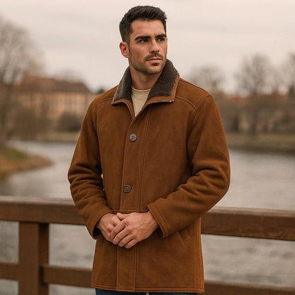 Man wearing a brown coat standing by a river with a blurred background