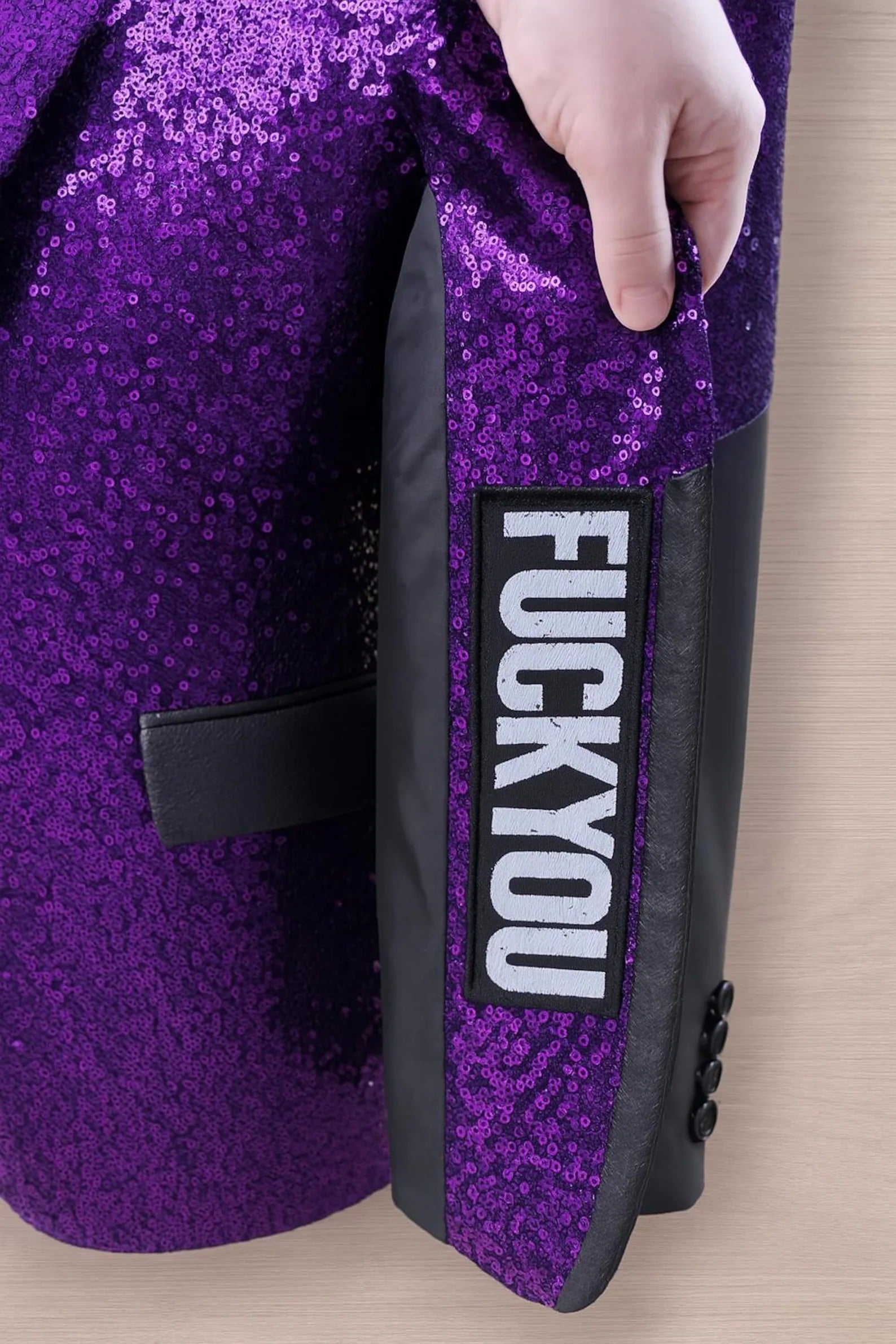 Purple sequin jacket with a 'FUCK YOU' patch on a wooden surface