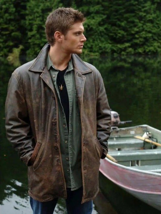 Man wearing a brown leather jacket by a boat on a body of water.