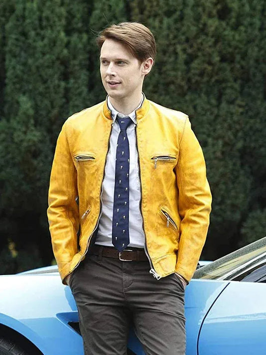 Man wearing a yellow jacket and blue tie standing next to a blue car with greenery in the background